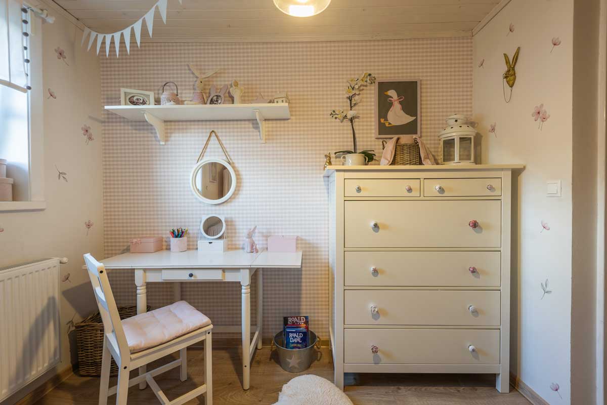 Dívčí pokoj s růžovými dekoracemi, bílým nábytkem a jemnou výmalbou s motivy květů.
