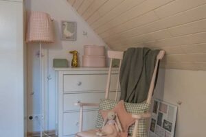 Růžová houpací židle s měkkými polštáři a plyšovým králíčkem v dívčím pokojíčku s venkovským kouzlem.