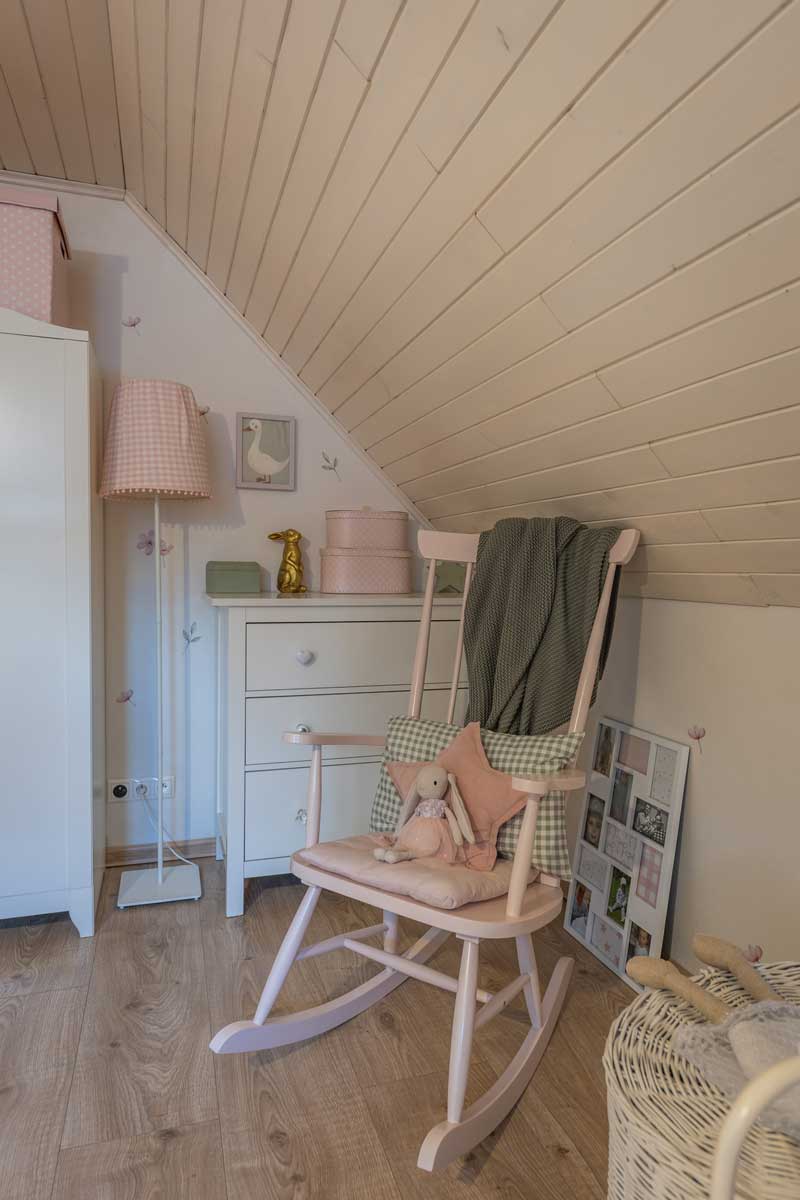 Růžová houpací židle s měkkými polštáři a plyšovým králíčkem v dívčím pokojíčku s venkovským kouzlem.