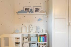 Dětský hrací koutek v jemných tónech s knihami, košíky a dekoracemi v podobě domečků a obláčků.