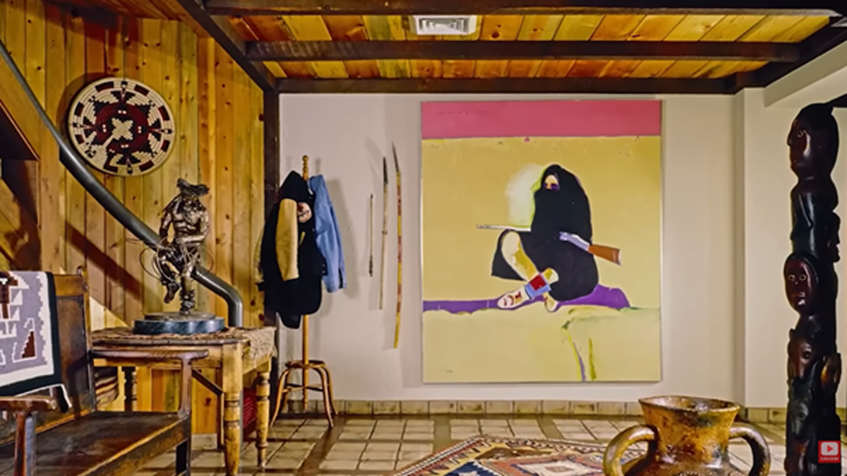 Interiér s dřevěným obložením, obrazem, sochou a dekoracemi inspirovanými původními kulturami.