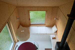 Pohled z horního patra odhaluje promyšlenou kompozici dřeva, světla a geometrie. Kombinace přirozeného obložení, bílých ploch a černých detailů vytváří dojem klidu a precizního řádu.