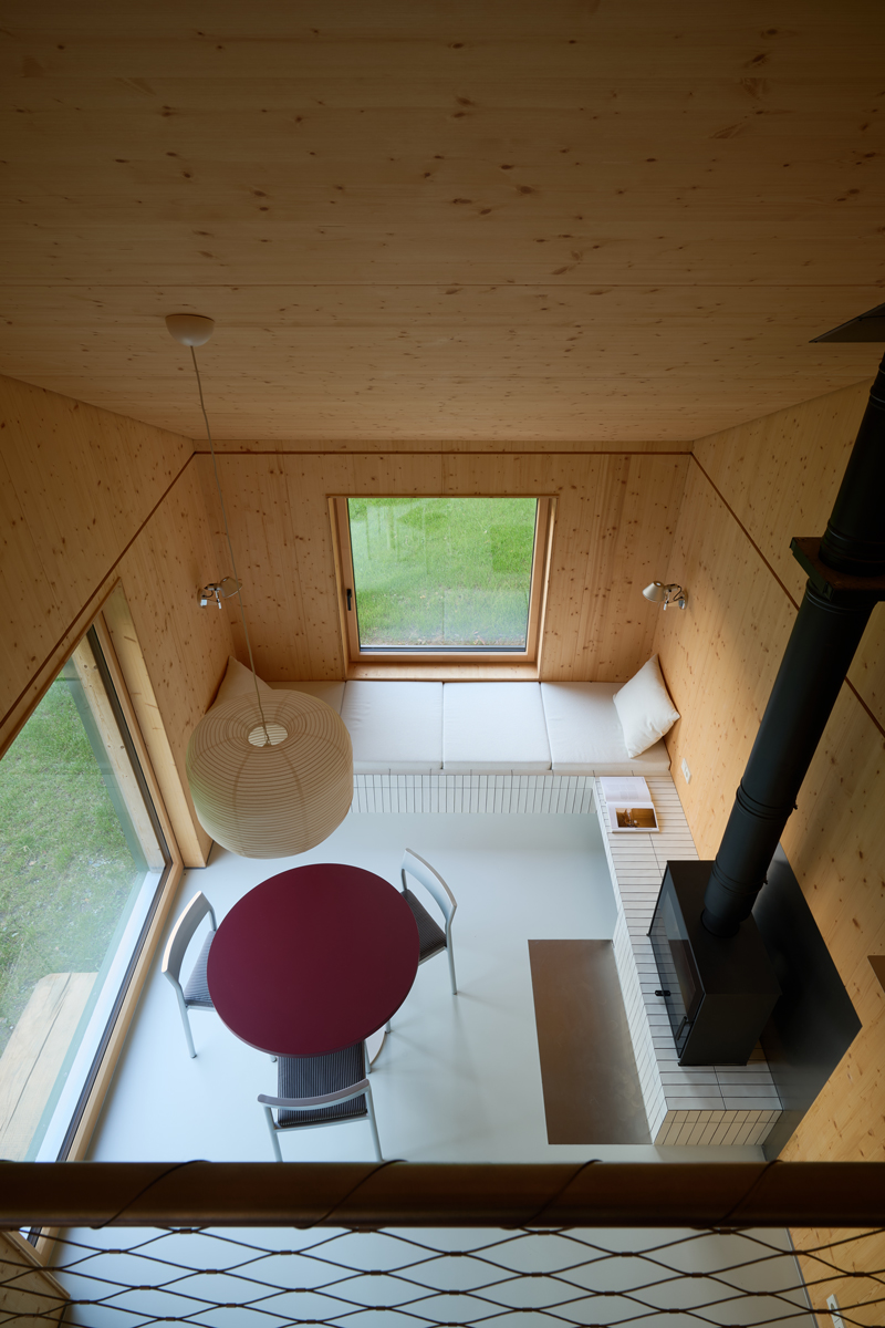 Pohled z horního patra odhaluje promyšlenou kompozici dřeva, světla a geometrie. Kombinace přirozeného obložení, bílých ploch a černých detailů vytváří dojem klidu a precizního řádu.