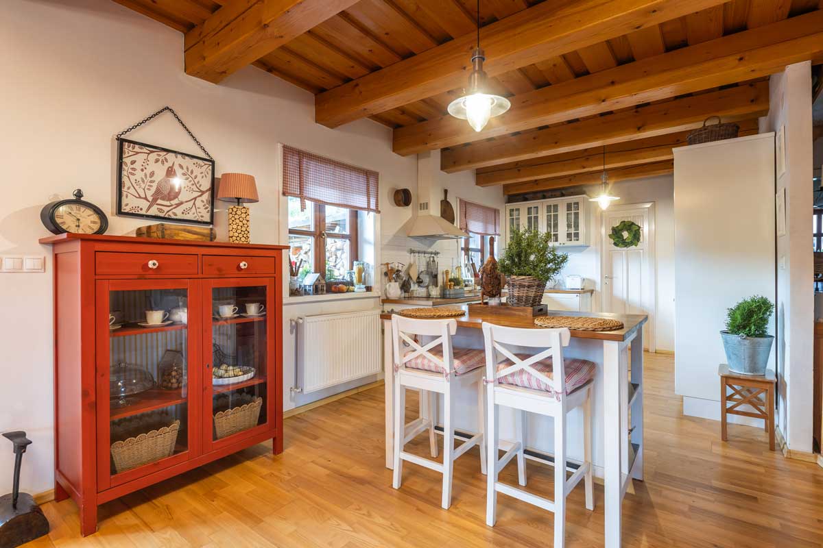 Jídelní kout s bílou kuchyní, barovým posezením a venkovskými detaily v podobě proutěných košíků a keramických dekorací.