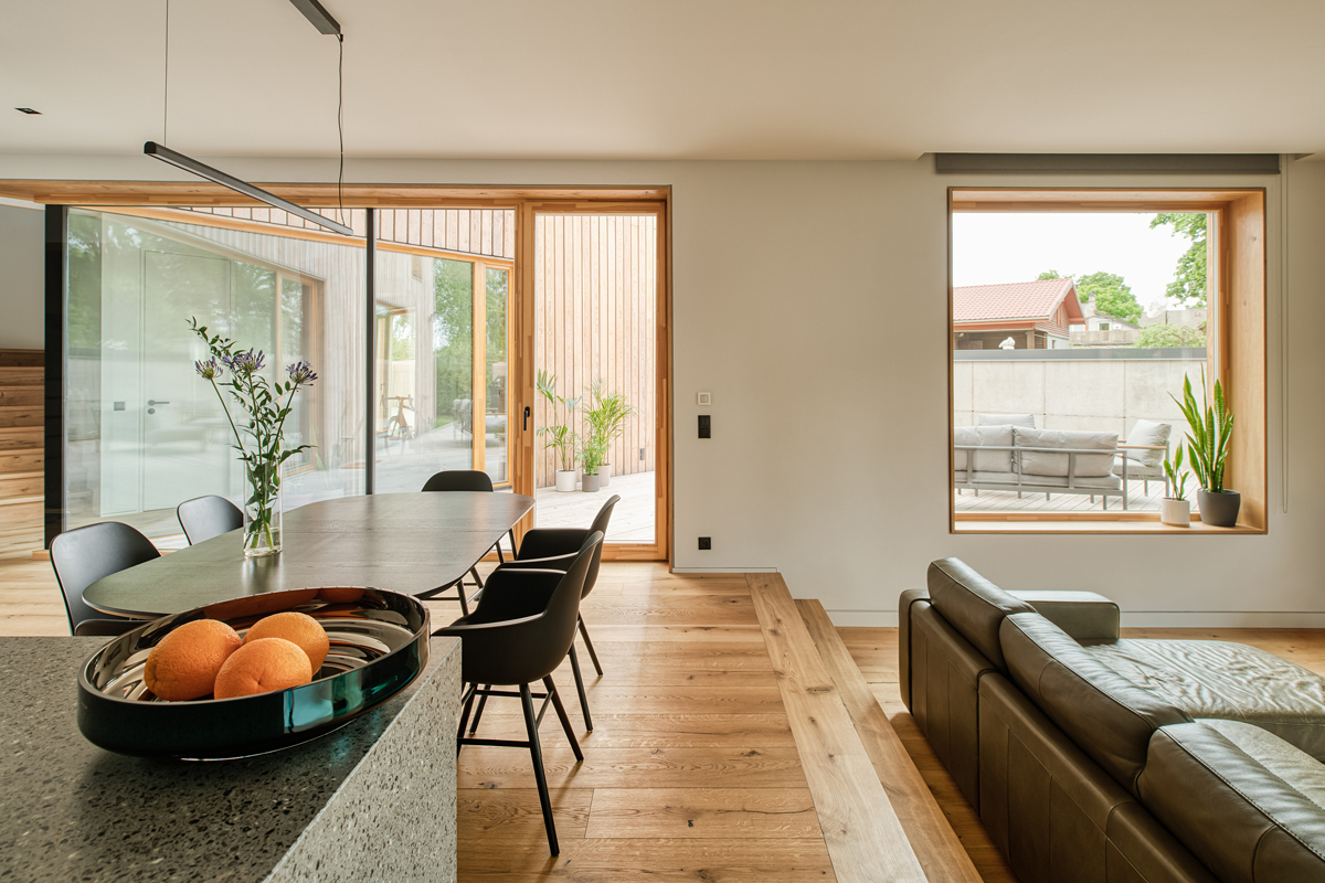 Jídelna s oválným stolem a kuchyňským ostrůvkem, otevřená do zahrady přes velká okna.