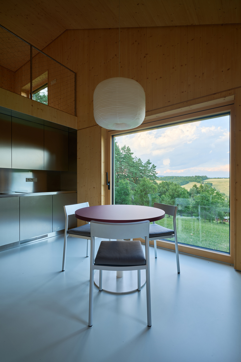 Moderní kuchyň a jídelní kout s kulatým stolem a výhledem do zelené krajiny.