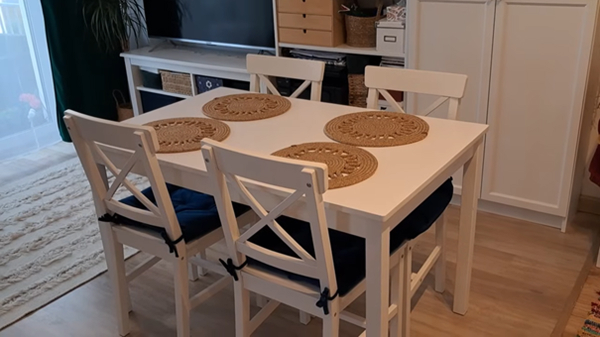 Bílý jídelní stůl se čtyřmi židlemi a kruhovými prostírkami z přírodního materiálu.