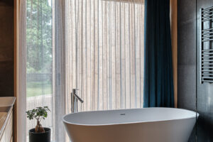 Koupelna s volně stojící vanou, průsvitným závěsem a tmavou podlahou.