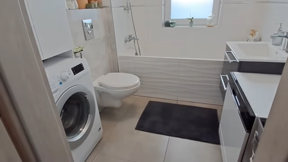 Moderní koupelna s vanou, pračkou a bílým nábytkem v malém bytě.