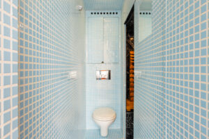 Úzká koupelna s tyrkysovým mozaikovým obkladem a závěsnou toaletou.