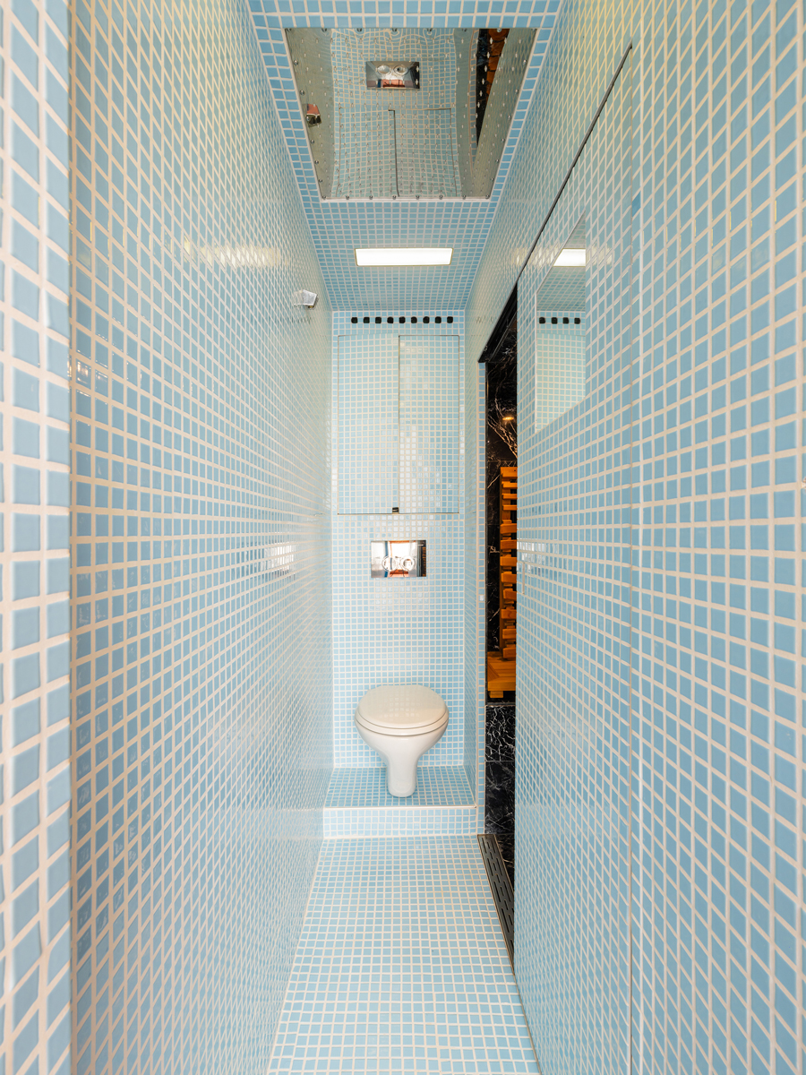 Úzká koupelna s tyrkysovým mozaikovým obkladem a závěsnou toaletou.