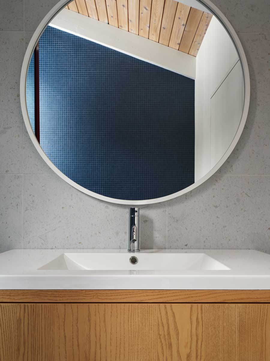 Minimalistický detail koupelnového zrcadla odhaluje střídmou kombinaci dřeva a dlaždic, navazující na celkový přírodní tón interiéru.