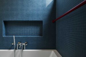 Tmavě modrá dlažba a jednoduché linie vodovodních prvků dodávají modernizované koupelně elegantní, uklidňující atmosféru.