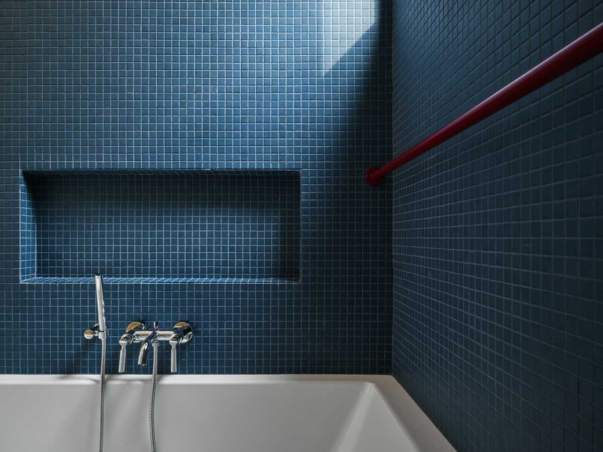 Tmavě modrá dlažba a jednoduché linie vodovodních prvků dodávají modernizované koupelně elegantní, uklidňující atmosféru.