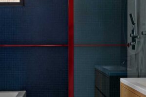 Moderní koupelna s tmavě modrou mozaikou a výraznými červenými detaily potvrzuje, že i horský dům může nabídnout odvážné a elegantní řešení.