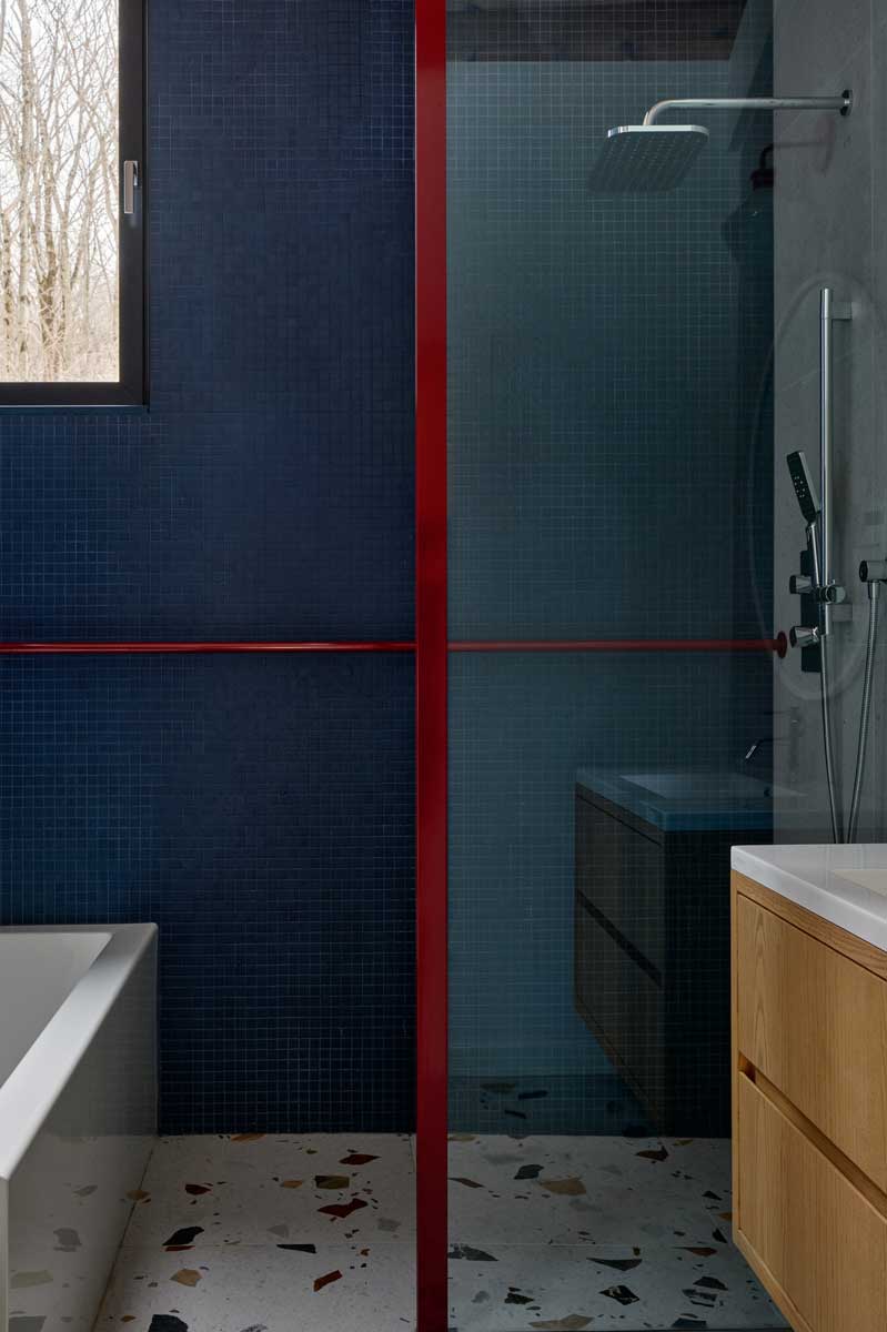 Moderní koupelna s tmavě modrou mozaikou a výraznými červenými detaily potvrzuje, že i horský dům může nabídnout odvážné a elegantní řešení.