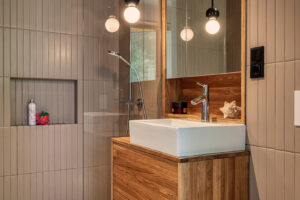 Koupelna s dřevěným umyvadlovým stolkem, sprchovým koutem a zrcadlem s kulatými svítidly.