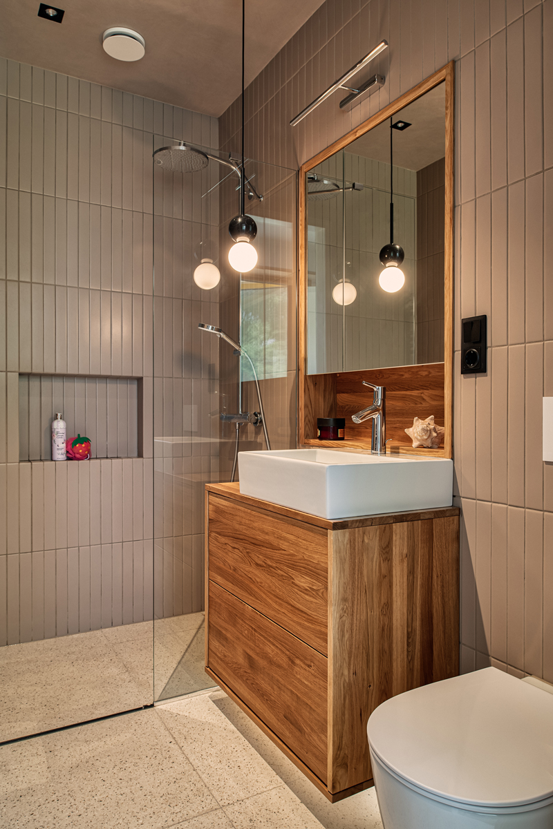 Koupelna s dřevěným umyvadlovým stolkem, sprchovým koutem a zrcadlem s kulatými svítidly.