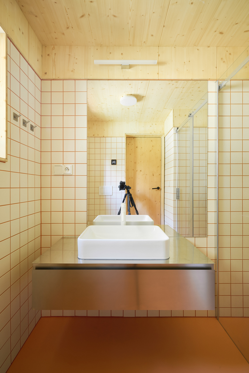 Moderní koupelna s dvojicí umyvadel, nerezovou deskou a oranžovými spárami.