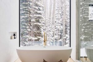 Volně stojící vana u velkého okna s výhledem na zasněžený les.