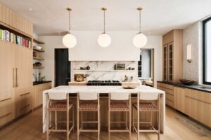 Světlá kuchyně s mramorovou pracovní deskou a závěsnými kulovými svítidly.