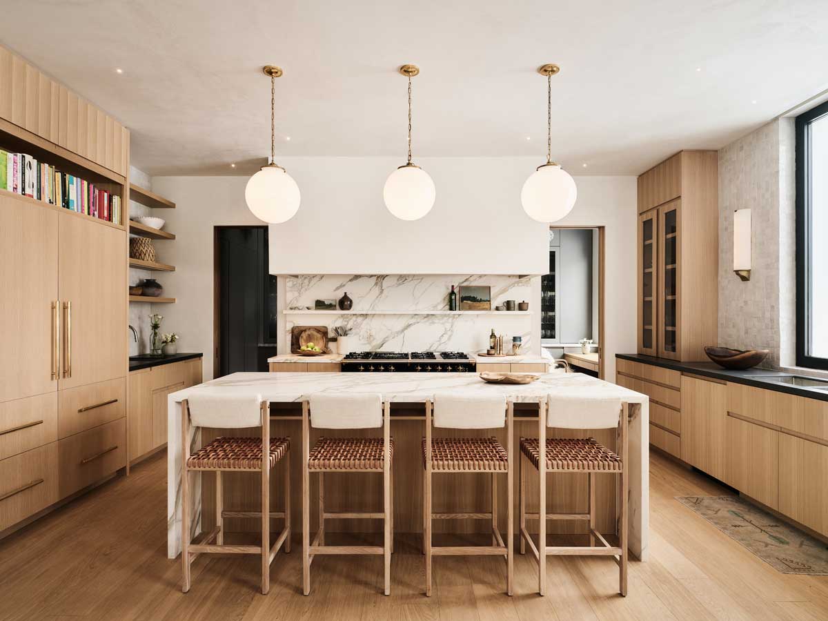 Světlá kuchyně s mramorovou pracovní deskou a závěsnými kulovými svítidly.