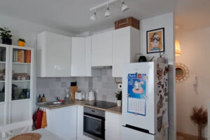 Malá bílá kuchyň s jídelním stolem a praktickým úložným prostorem v moderním bytě.