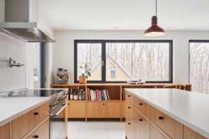 Světlá a vzdušná kuchyně s velkými okny otevírá interiér směrem k lesu a stává se přirozeným centrem rodinného života.