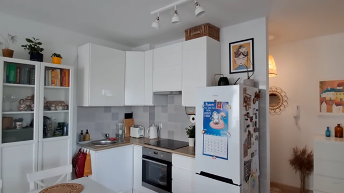 Malá bílá kuchyň s jídelním stolem a praktickým úložným prostorem v moderním bytě.