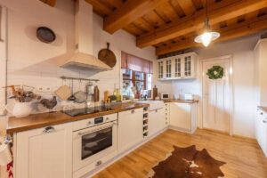 Bílá kuchyňská linka s dřevěnou deskou a otevřenými policemi.