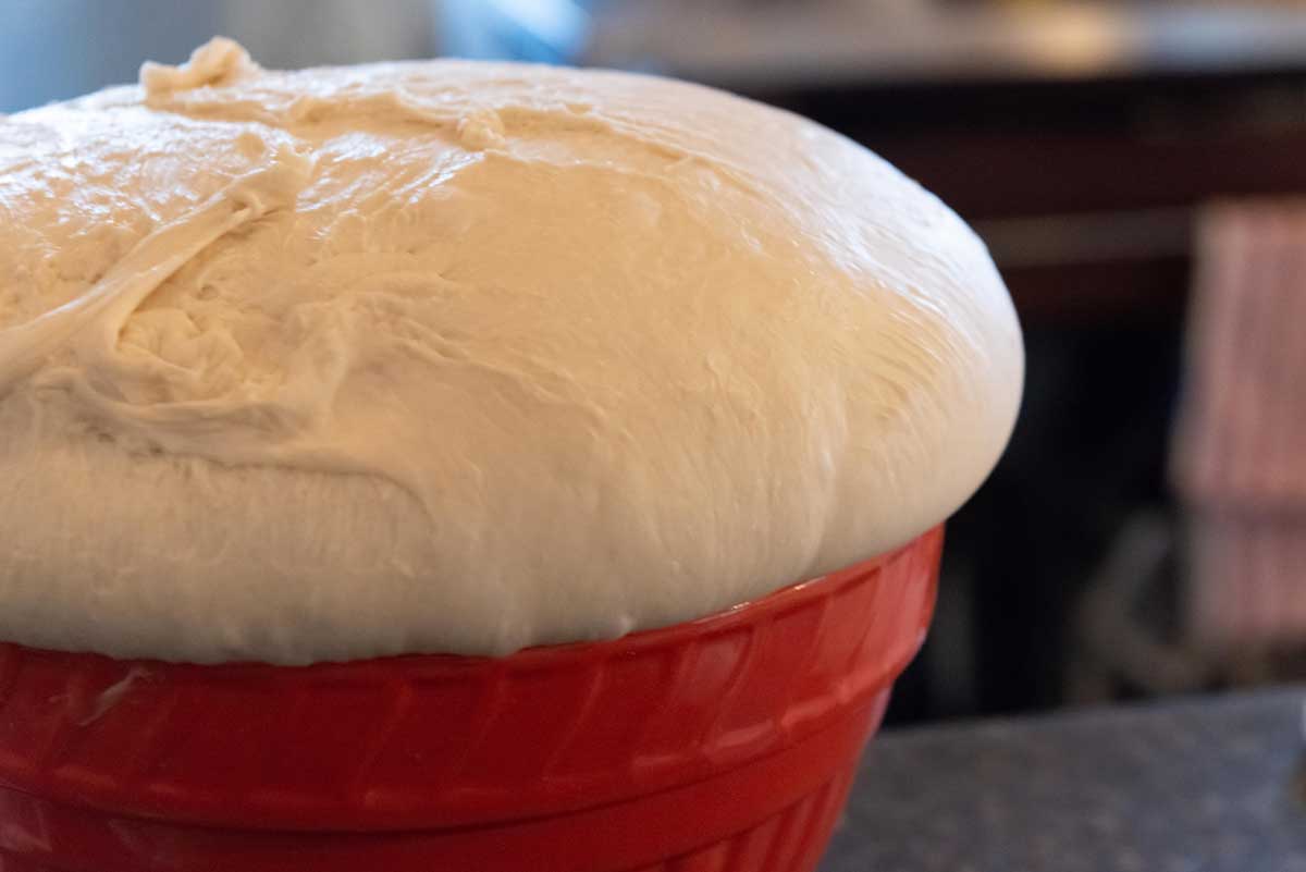 Překynuté těsto v červené míse ukazující, jak výrazně může těsto při správném kynutí zvětšit objem.