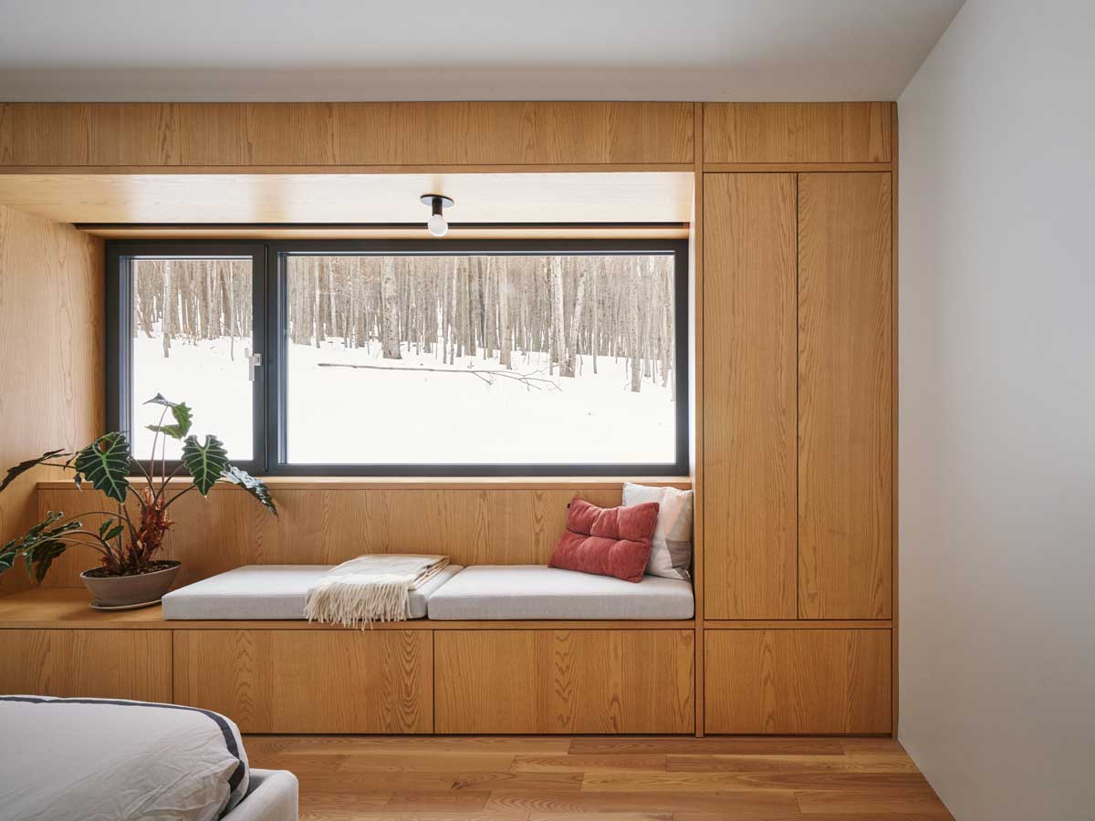 Vestavěná lavice pod širokým oknem nabízí klidné místo k odpočinku, odkud lze pozorovat proměny horské krajiny během celého roku.