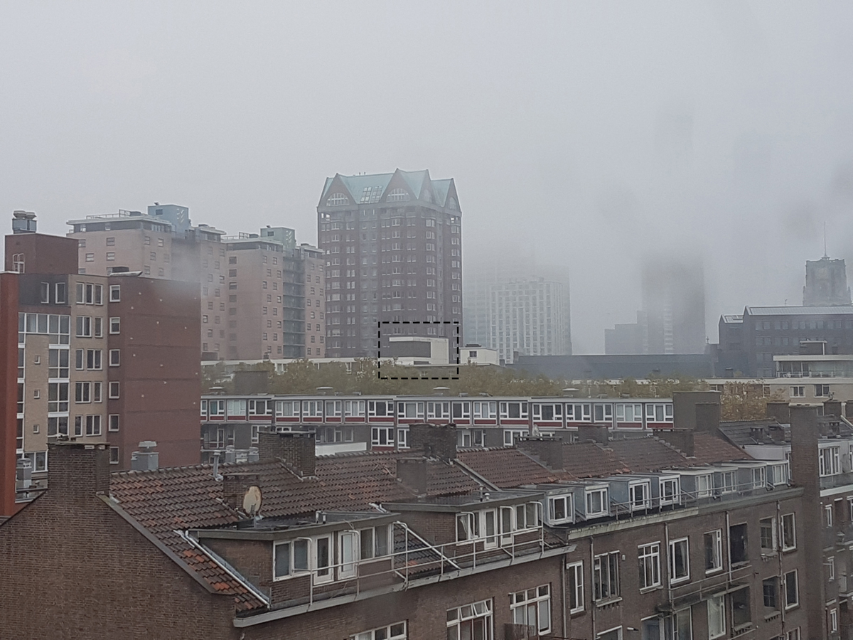 Pohled na městskou zástavbu v mlze s vyššími budovami v pozadí.