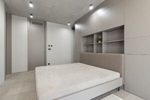 Ložnice s čalouněným čelem postele a integrovaným úložným systémem v klidné barevnosti.