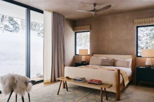 Ložnice s přírodní barevnou paletou a výhledem na zimní krajinu.