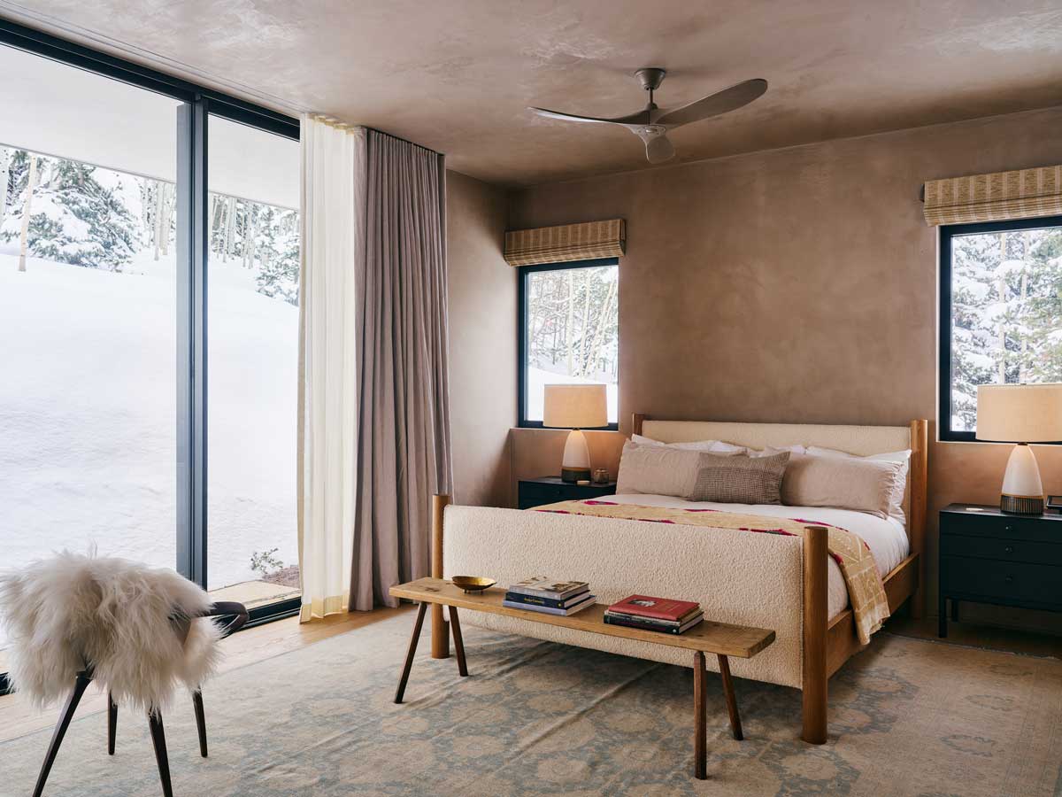 Ložnice s přírodní barevnou paletou a výhledem na zimní krajinu.