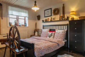 Venkovská ložnice s tmavým rámem postele a dekoracemi z přírodních materiálů.