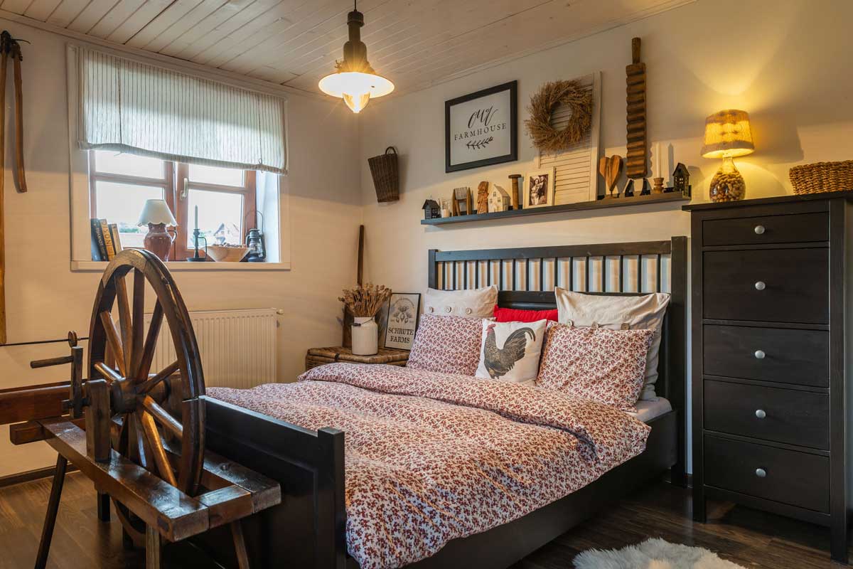 Venkovská ložnice s tmavým rámem postele a dekoracemi z přírodních materiálů.