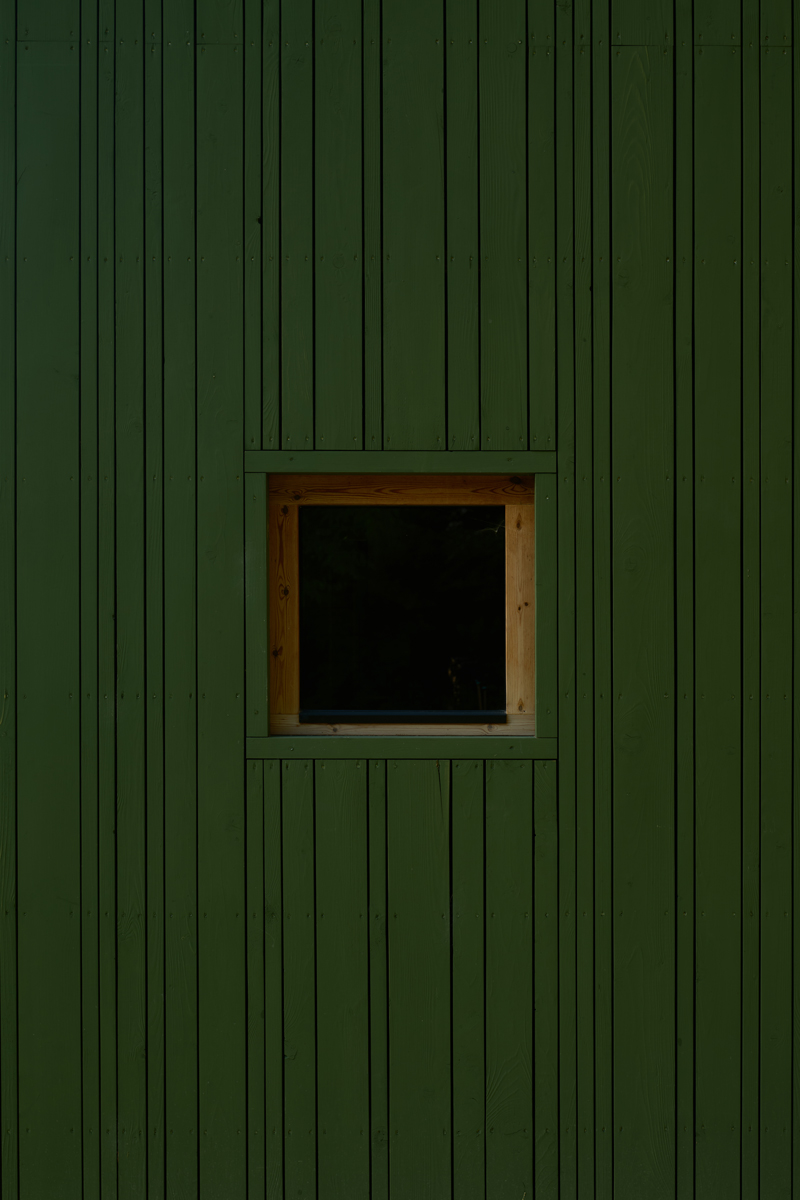 Detail zelené fasády s malým dřevěným oknem.