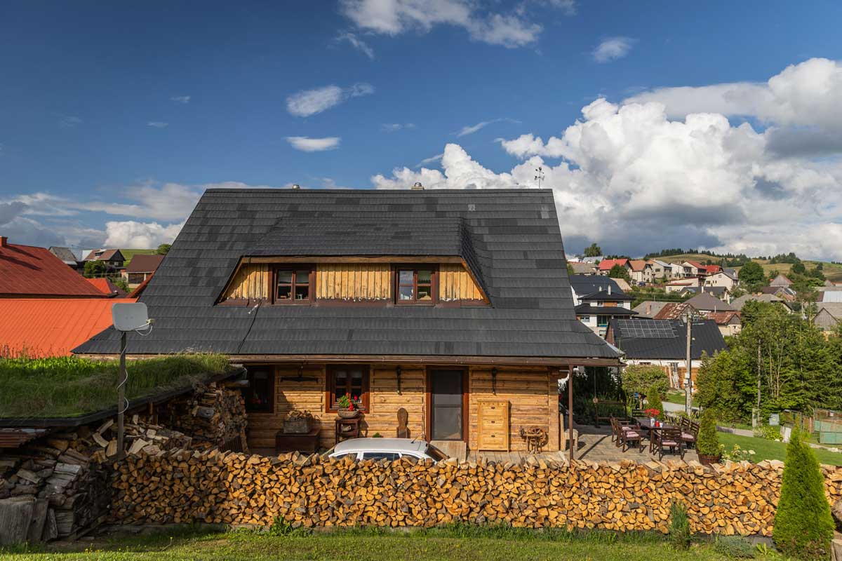 Pohled na moderní roubenku se šindelovou střechou a dřevěnou terasou v horské vesnici.