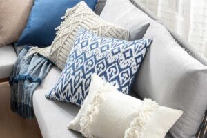 Detail dekorativních modrých a krémových polštářů na světlé sedačce, které dodávají prostoru jemnou eleganci.