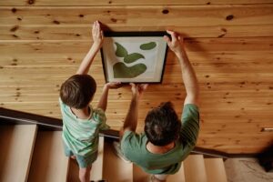 Otec se synem věší obraz na dřevěnou stěnu.