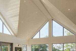 Obyvací pokoj s vysokými prosklenými stěnami zapojuje krajinu do interiéru a během dne mění atmosféru podle světla