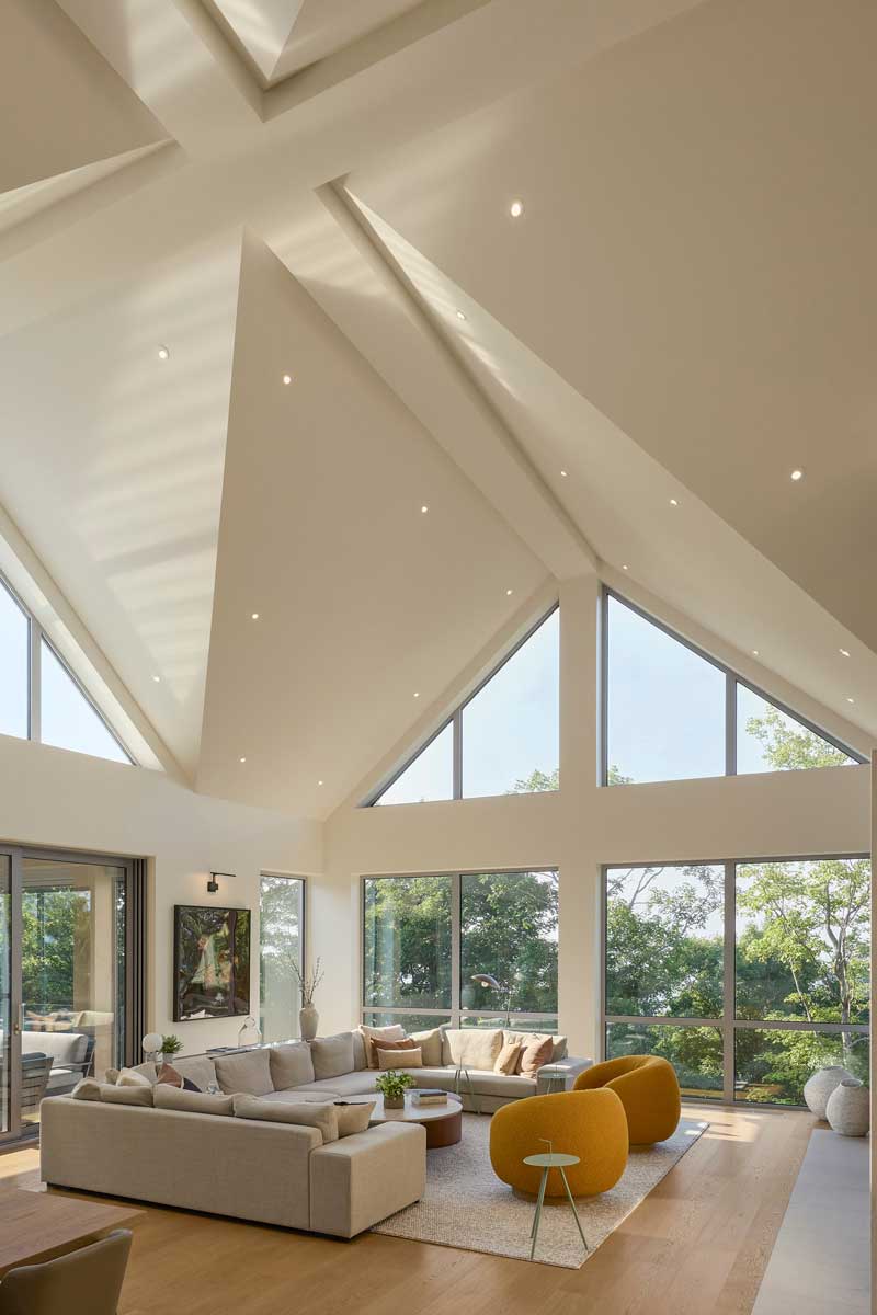 Obyvací pokoj s vysokými prosklenými stěnami zapojuje krajinu do interiéru a během dne mění atmosféru podle světla