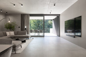 Otevřený obývací pokoj s šedou rohovou sedačkou a výhledem na terasu.