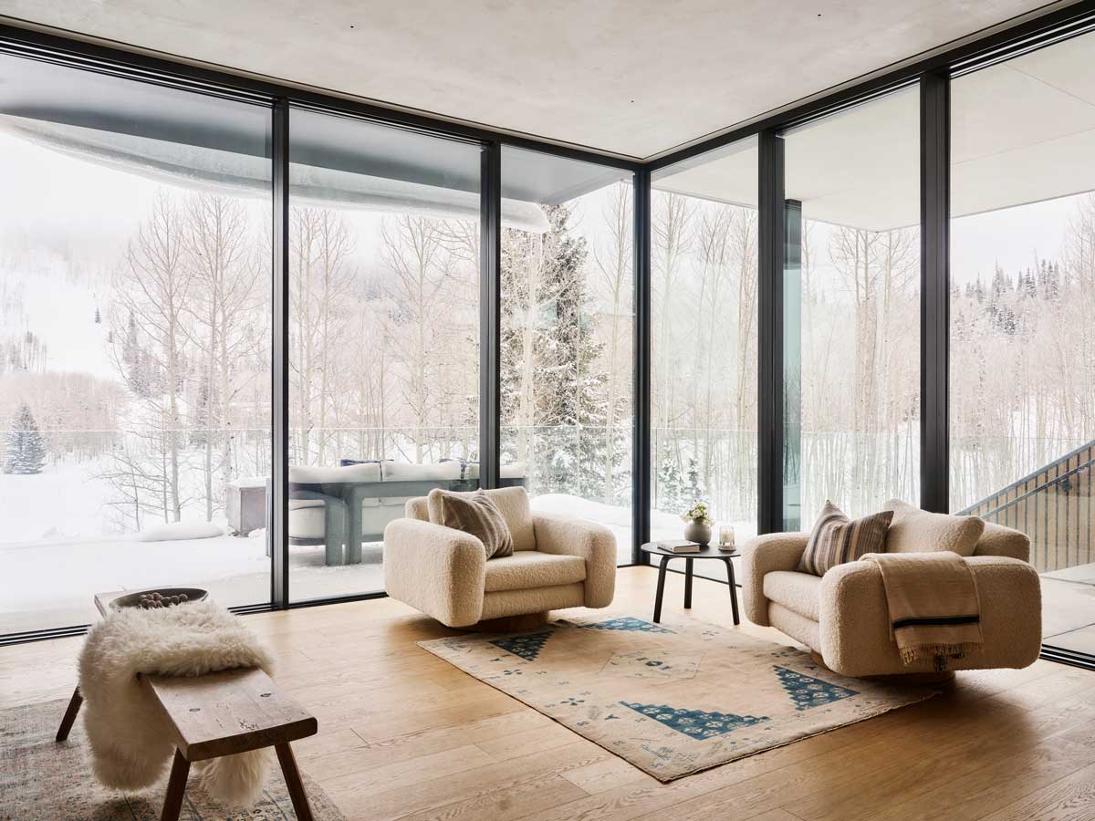 Roh obývacího pokoje s čalouněnými křesly a výhledem na les.