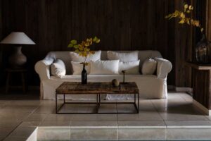 Odpočinková část u bazénu v Chalet 1936 s bílou pohovkou, recyklovaným dřevěným stolkem a přírodními dekoracemi.