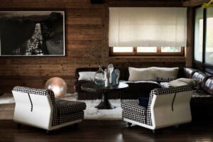 Interiér Chalet 1936 s vintage křesly, koženou sedačkou a stěnami z recyklovaného alpského dřeva.