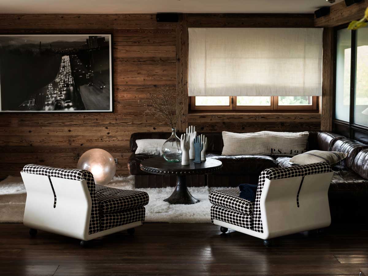 Interiér Chalet 1936 s vintage křesly, koženou sedačkou a stěnami z recyklovaného alpského dřeva.