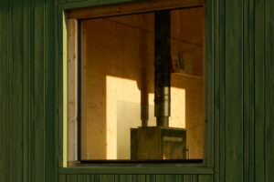 Detail tmavozelené fasády chaty Bebech s malým čtvercovým oknem ukazuje jednoduchost a dokonalé řemeslo.